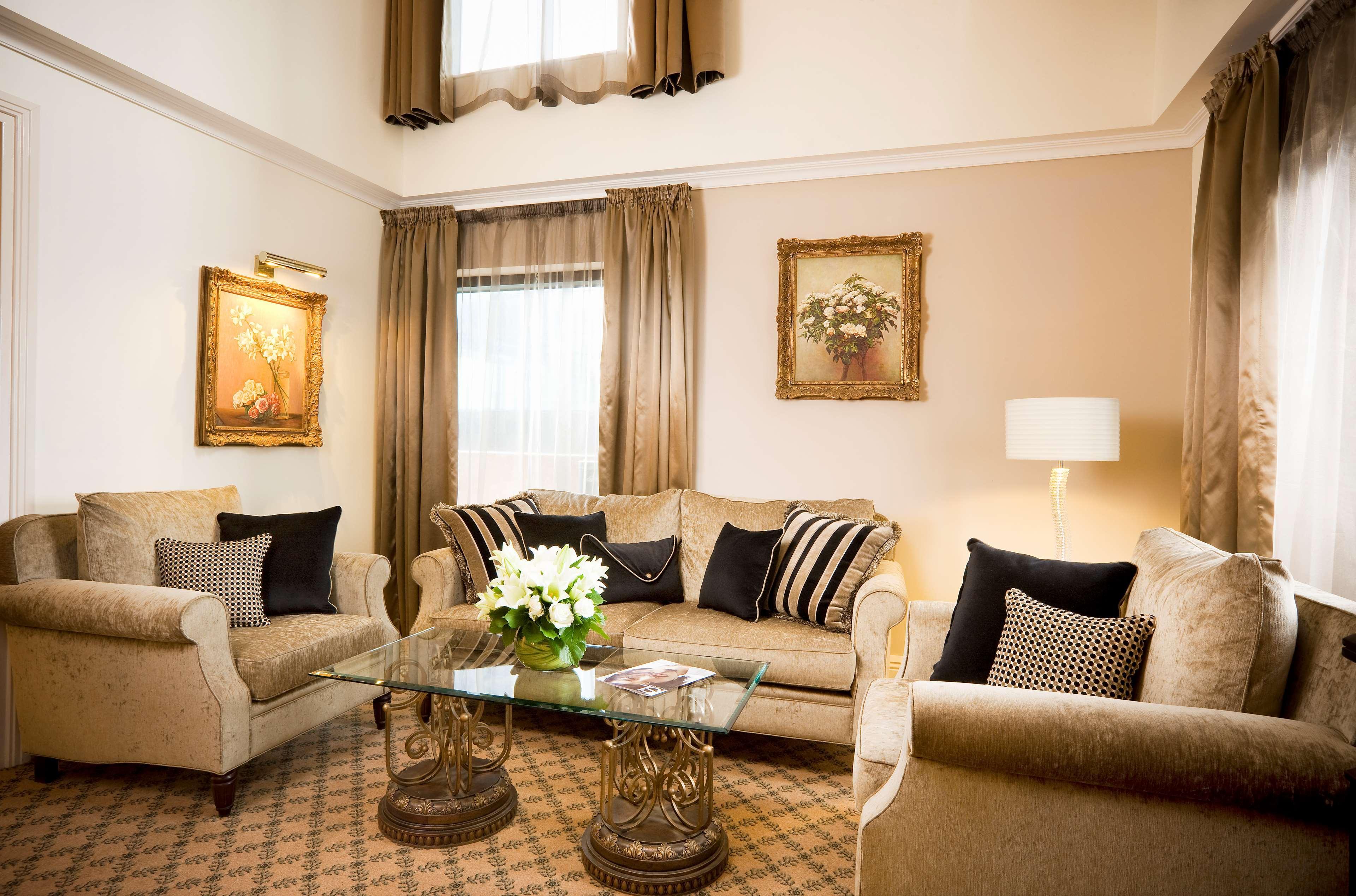 מלון Stamford Plaza מלבורן חדר תמונה The photo depicts a stylish living room with a warm and inviting aesthetic. It features a set of comfortable beige sofas adorned with decorative pillows in black and patterned designs. There is a glass coffee table at the center, supported by elegant