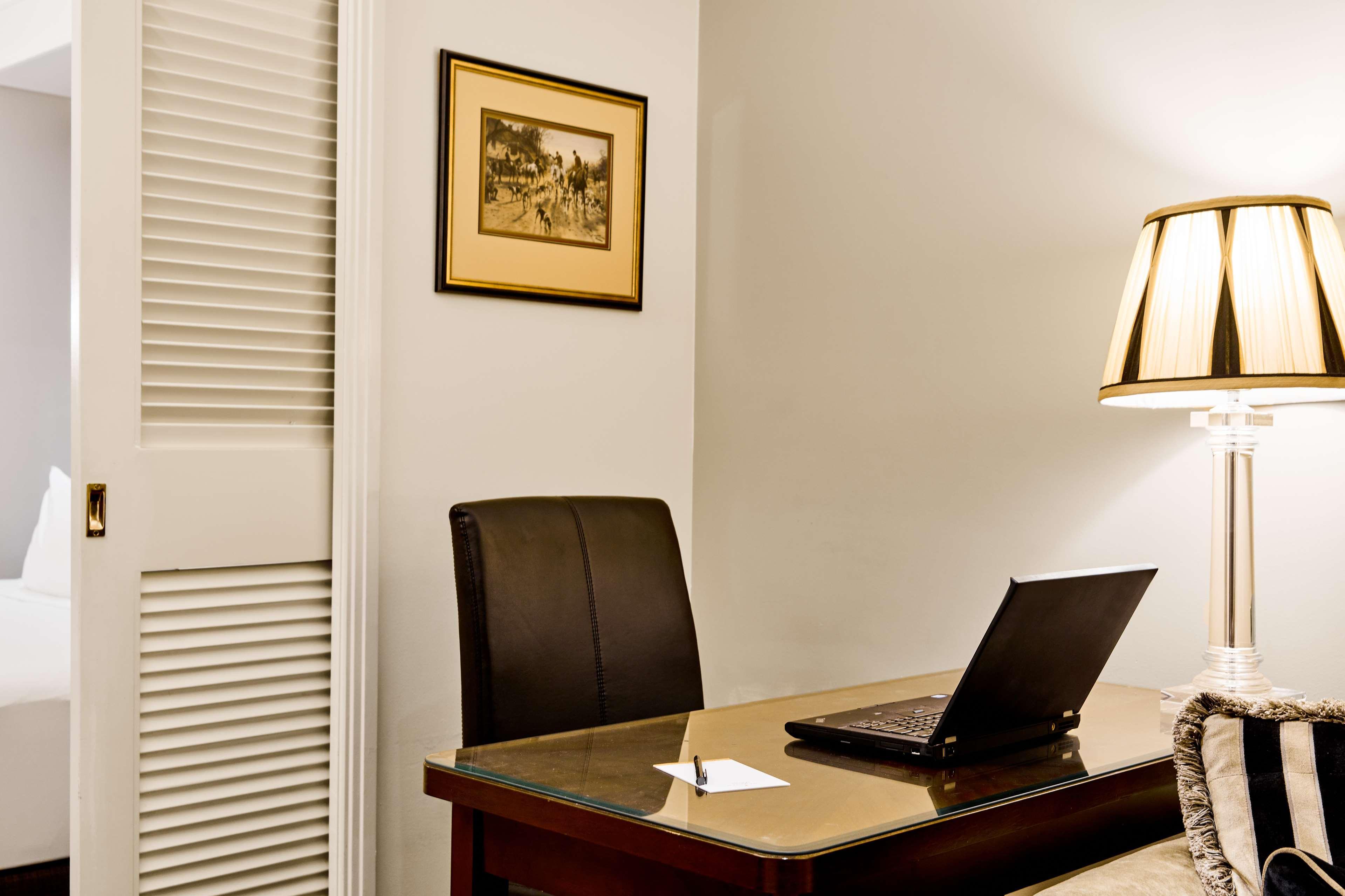 מלון Stamford Plaza מלבורן מראה חיצוני תמונה The photo shows a small office or workspace. There is a desk with a glass surface, and on it sits a laptop computer. A piece of paper or notecard is also placed on the desk. Behind the desk is a black office chair. A wall lamp with a striped shade is