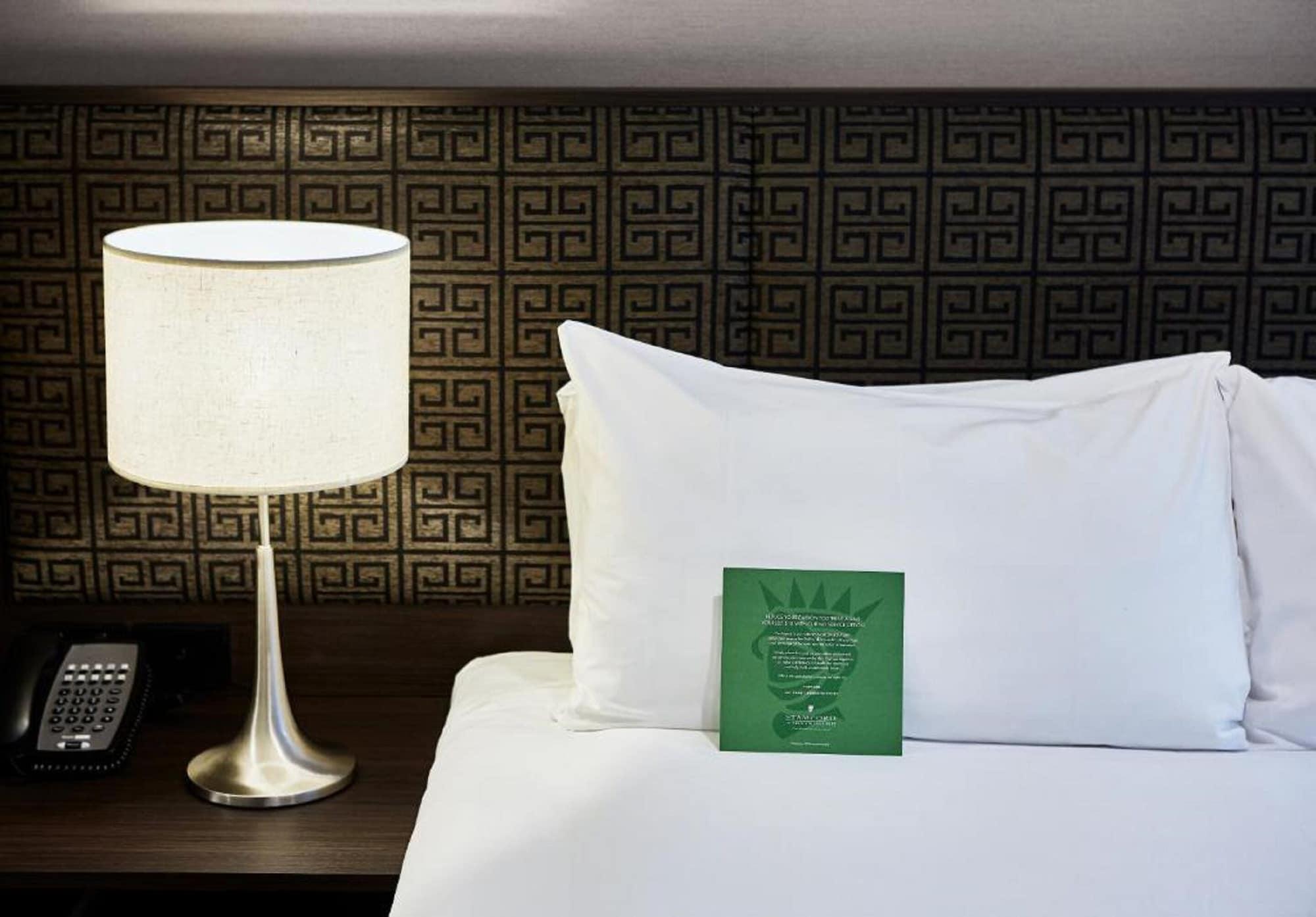 מלון Stamford Plaza מלבורן מראה חיצוני תמונה The photo shows a neatly made bed with a white pillow and a green item placed on top of it. Next to the bed, there is a stylish table lamp with a lampshade that appears to be white. In the background, you can see a patterned wall, which has a geometr