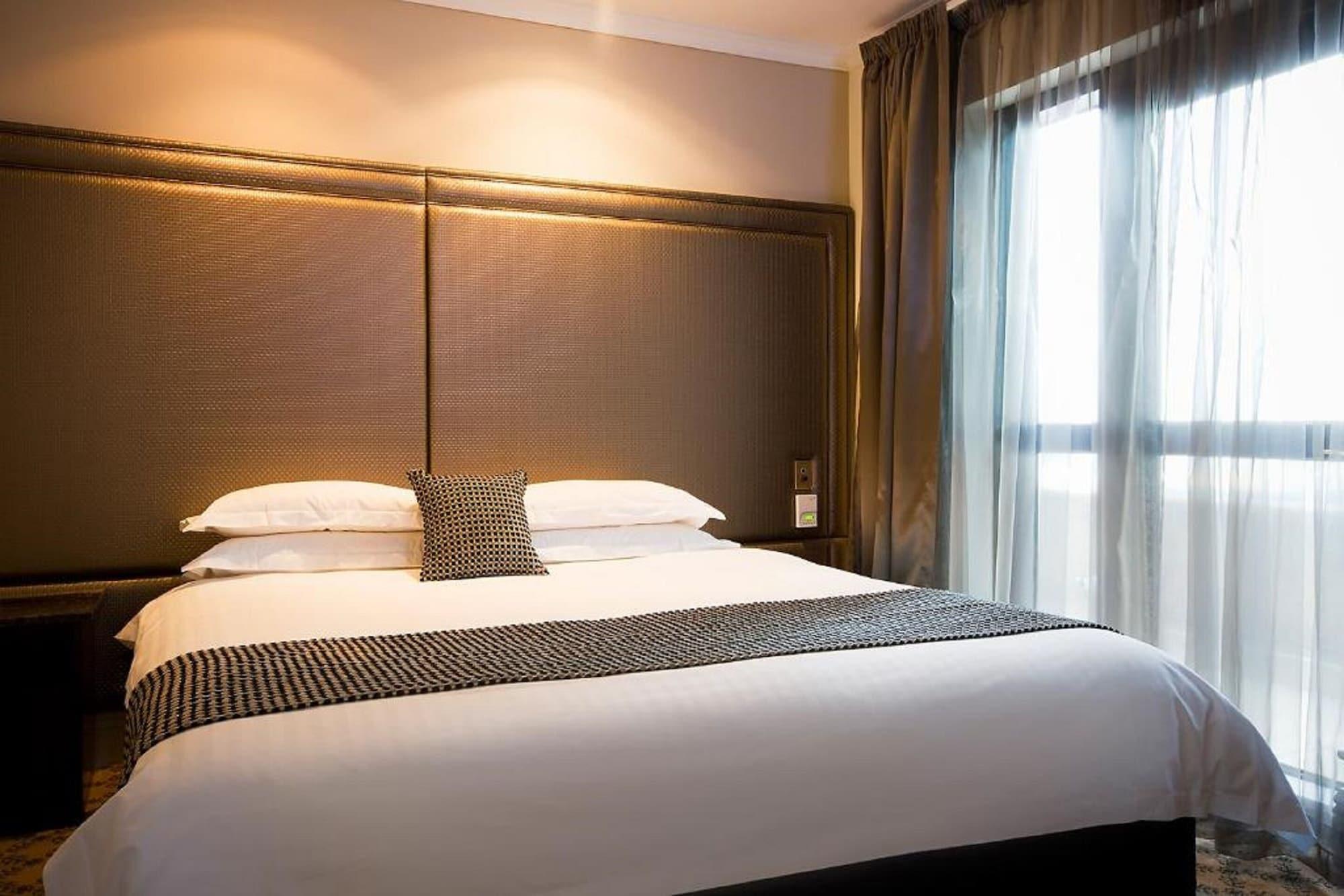 מלון Stamford Plaza מלבורן מראה חיצוני תמונה The photo shows a modern bedroom featuring a large bed with a neatly arranged white comforter and decorative pillows. The headboard is upholstered in a dark material, and there is soft lighting above it. On one side of the bed, there’s a small decora