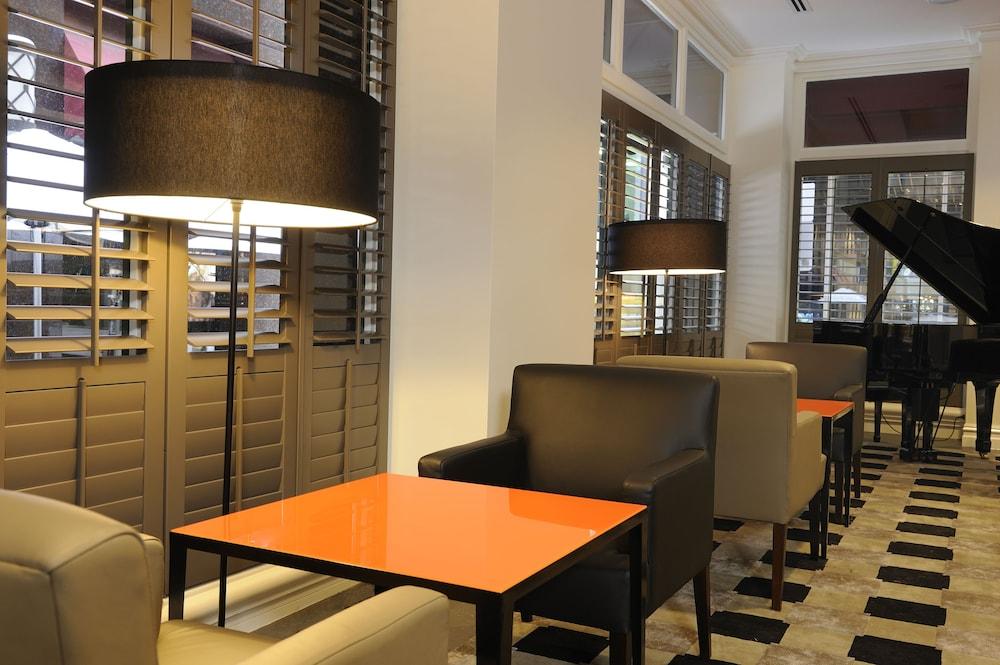 מלון Stamford Plaza מלבורן מראה חיצוני תמונה The photo shows a cozy interior space, likely a lounge or café. It features a modern design with a mix of seating options, including black and light-colored chairs surrounding small tables. One table has a bright orange top, creating a striking visua