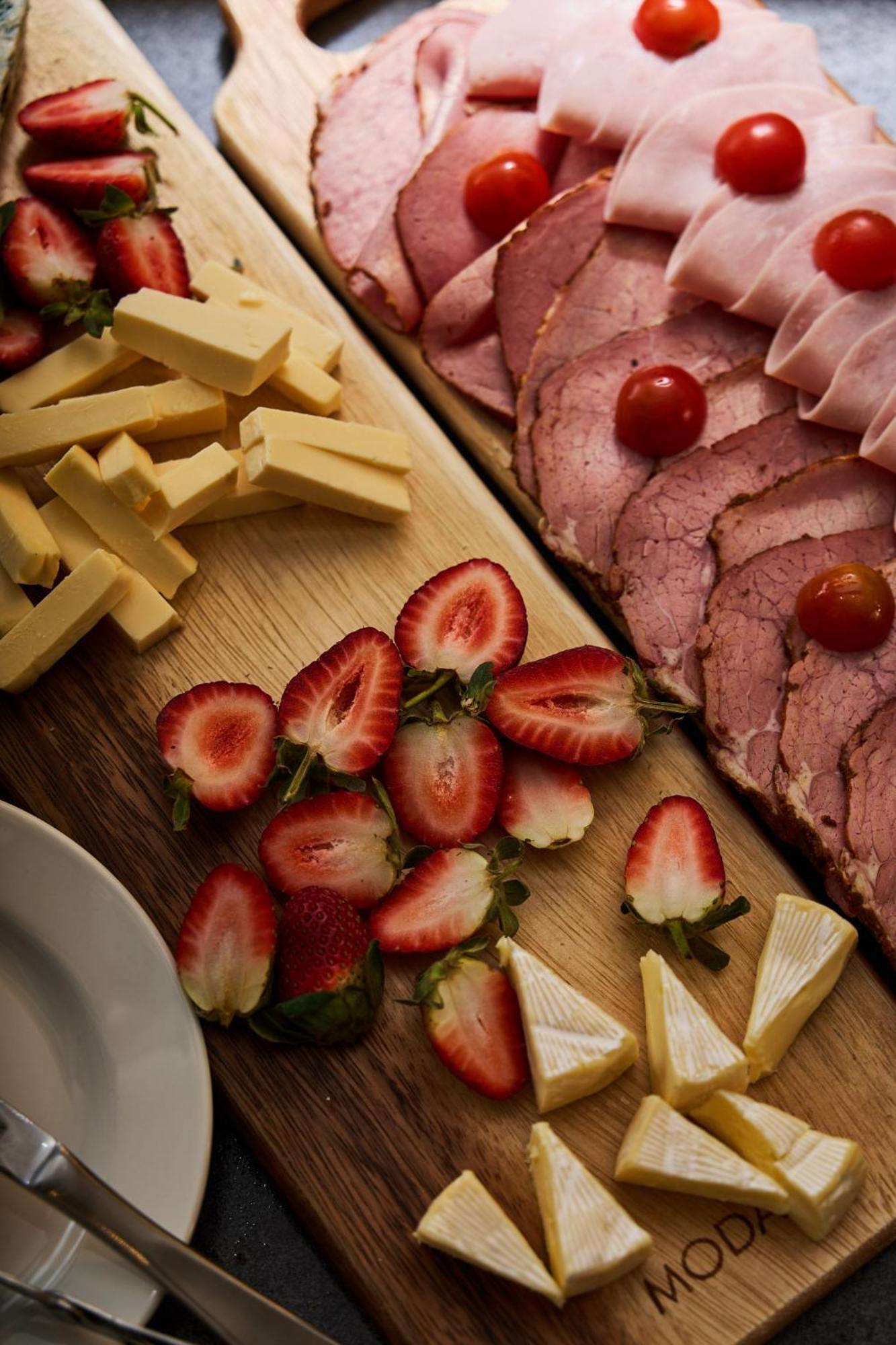 מלון Stamford Plaza מלבורן מראה חיצוני תמונה The photo displays an assortment of food items arranged on a wooden surface. There are slices of various meats, including ham, alongside round cherry tomatoes. Next to the meat, there are several pieces of yellow cheese cut into sticks. Additionally,