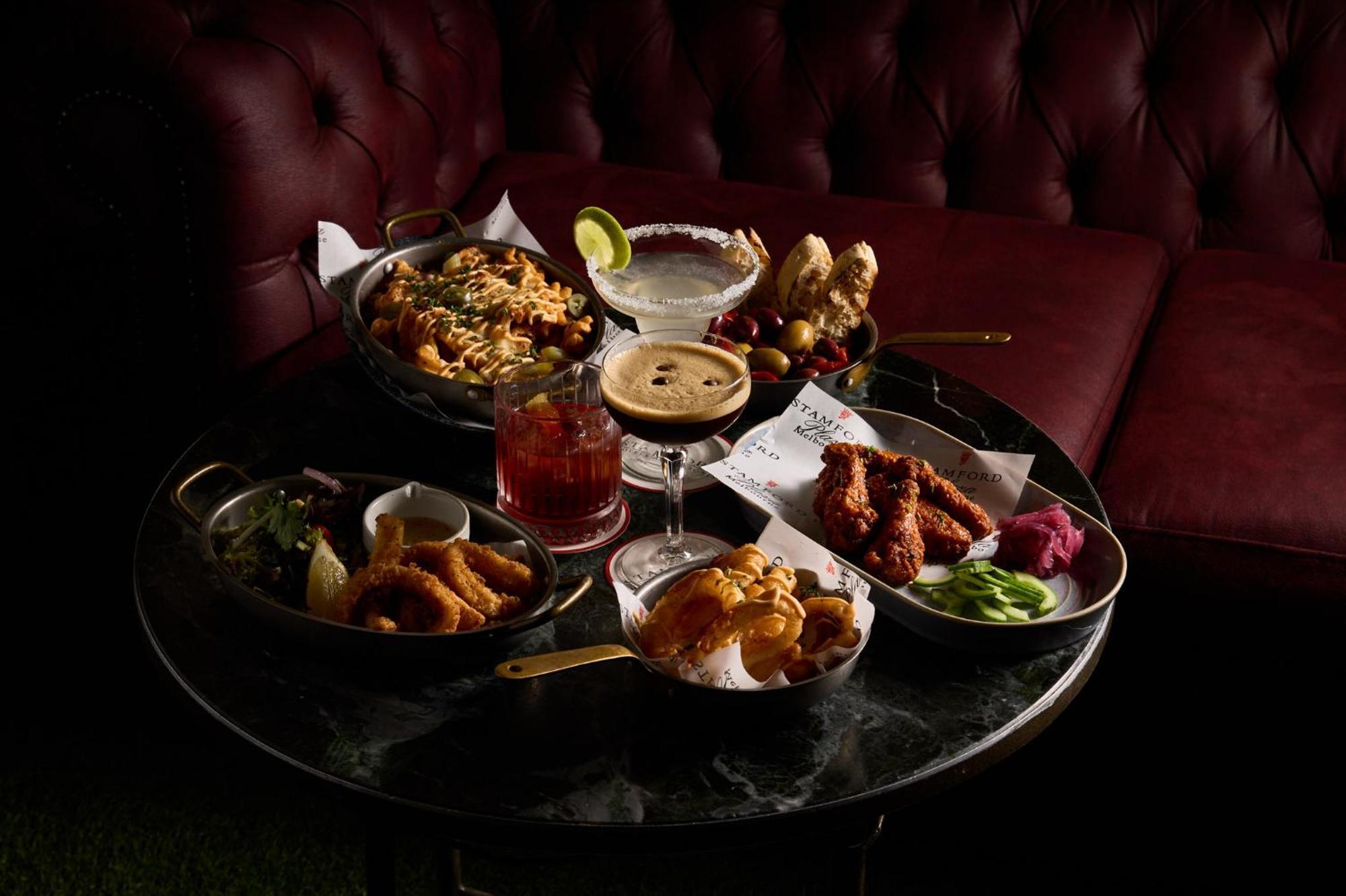 מלון Stamford Plaza מלבורן מראה חיצוני תמונה The photo showcases a variety of delicious foods and drinks arranged on a dark marble table. There are several dishes including:

1. A large bowl of pasta with a creamy sauce.
2. A platter of chicken wings, likely spicy or barbecued.
3. A small salad
