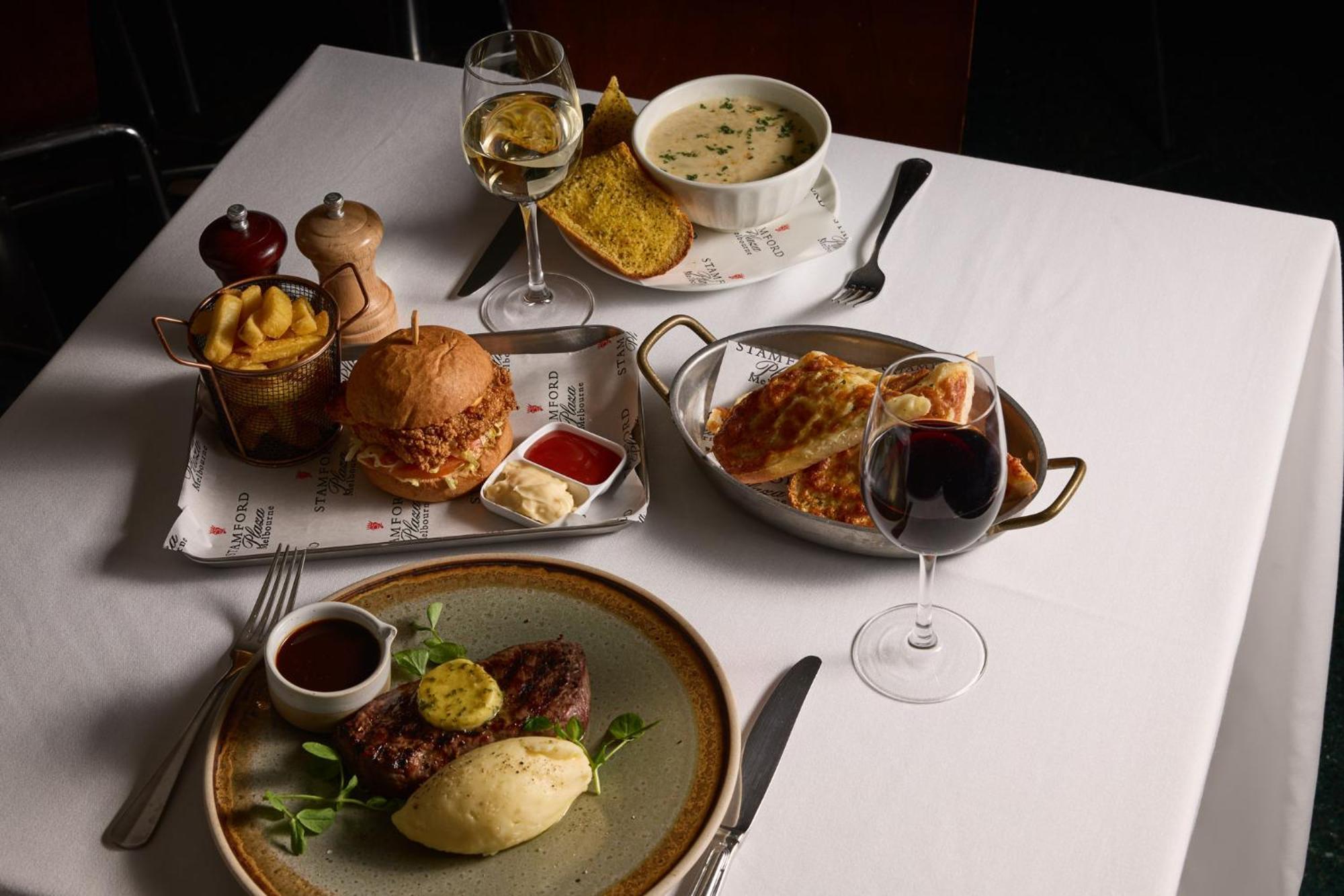 מלון Stamford Plaza מלבורן מראה חיצוני תמונה The photo showcases a variety of food and drinks arranged on a table set with a white tablecloth. 

1. **Main Dish:** A plate features a portion of steak topped with a slice of butter, accompanied by mashed potatoes and a garnish of greenery.
2. **Bu