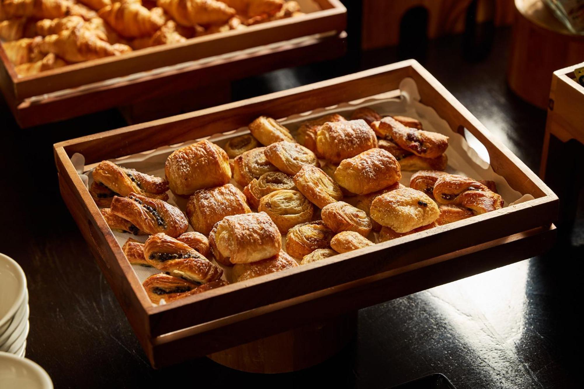 מלון Stamford Plaza מלבורן מראה חיצוני תמונה The photo shows a wooden tray filled with an assortment of baked goods. There are various types of pastries, including small, flaky items that appear to be puff pastries, and possibly some filled with chocolate or fruit. The pastries are golden brown