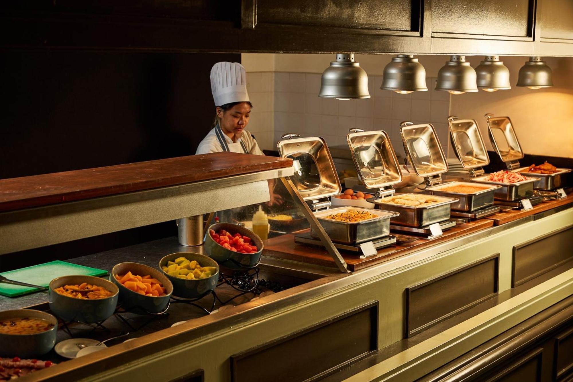 מלון Stamford Plaza מלבורן מראה חיצוני תמונה The photo shows a buffet setup in a dining area. There is a chef in a white uniform and hat, standing behind a counter filled with various food options. The buffet features several metal serving trays containing different dishes, with warming lights 