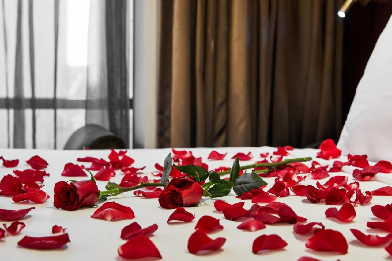 מלון Stamford Plaza מלבורן מראה חיצוני תמונה The photo shows a bed or a table covered with scattered red rose petals. Among the petals, there are a few whole red roses, still with their stems. The background features curtains that appear to be sheer, allowing some light to come through, and the